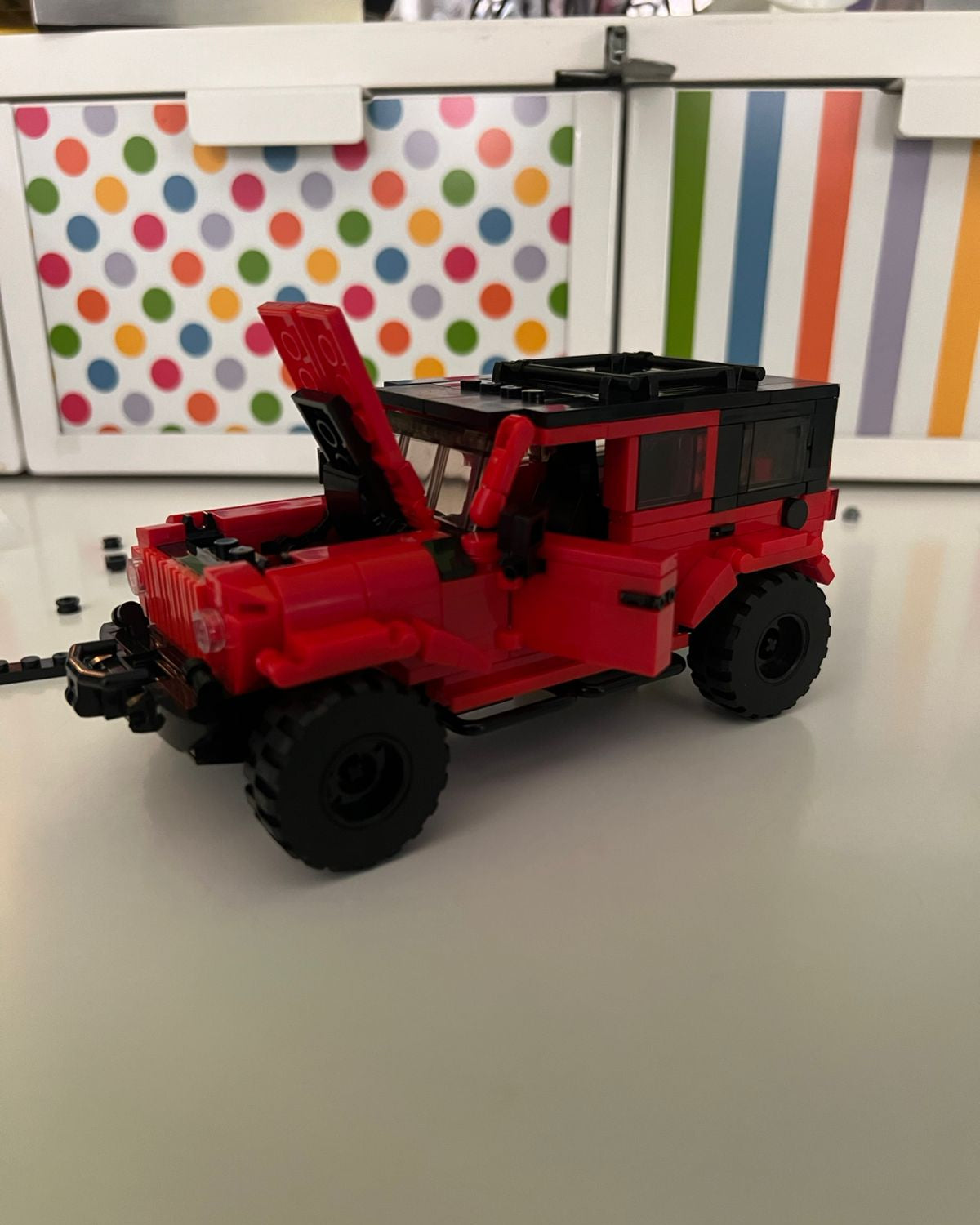 Red toy jeep on a plain background with colorful polka dot and striped patterns in the background.