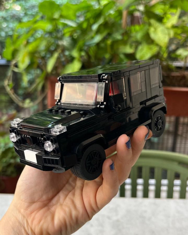 Black toy truck held in a hand with a blurred green outdoor background