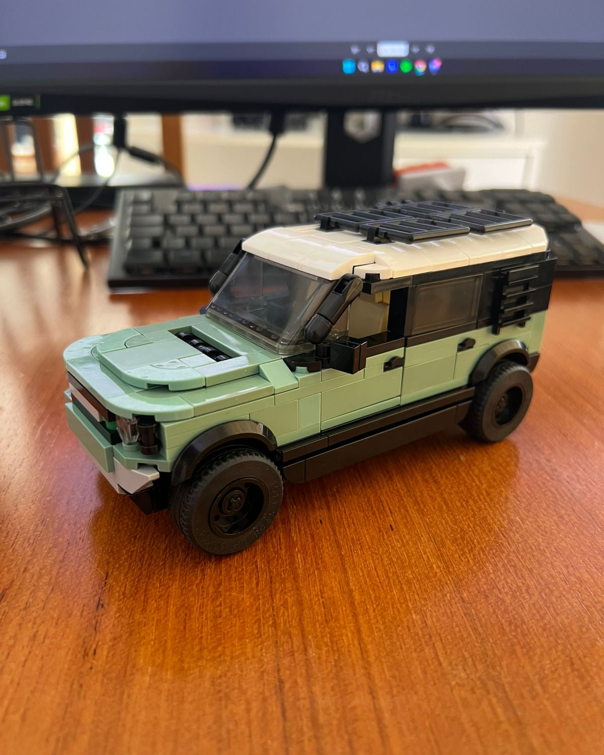 Toy car model on a wooden desk with a computer monitor in the background